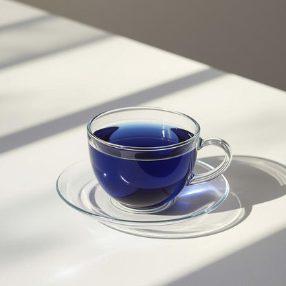 Clear glass tea cup with blue butterfly pea flower tea on a white surface with shadows
